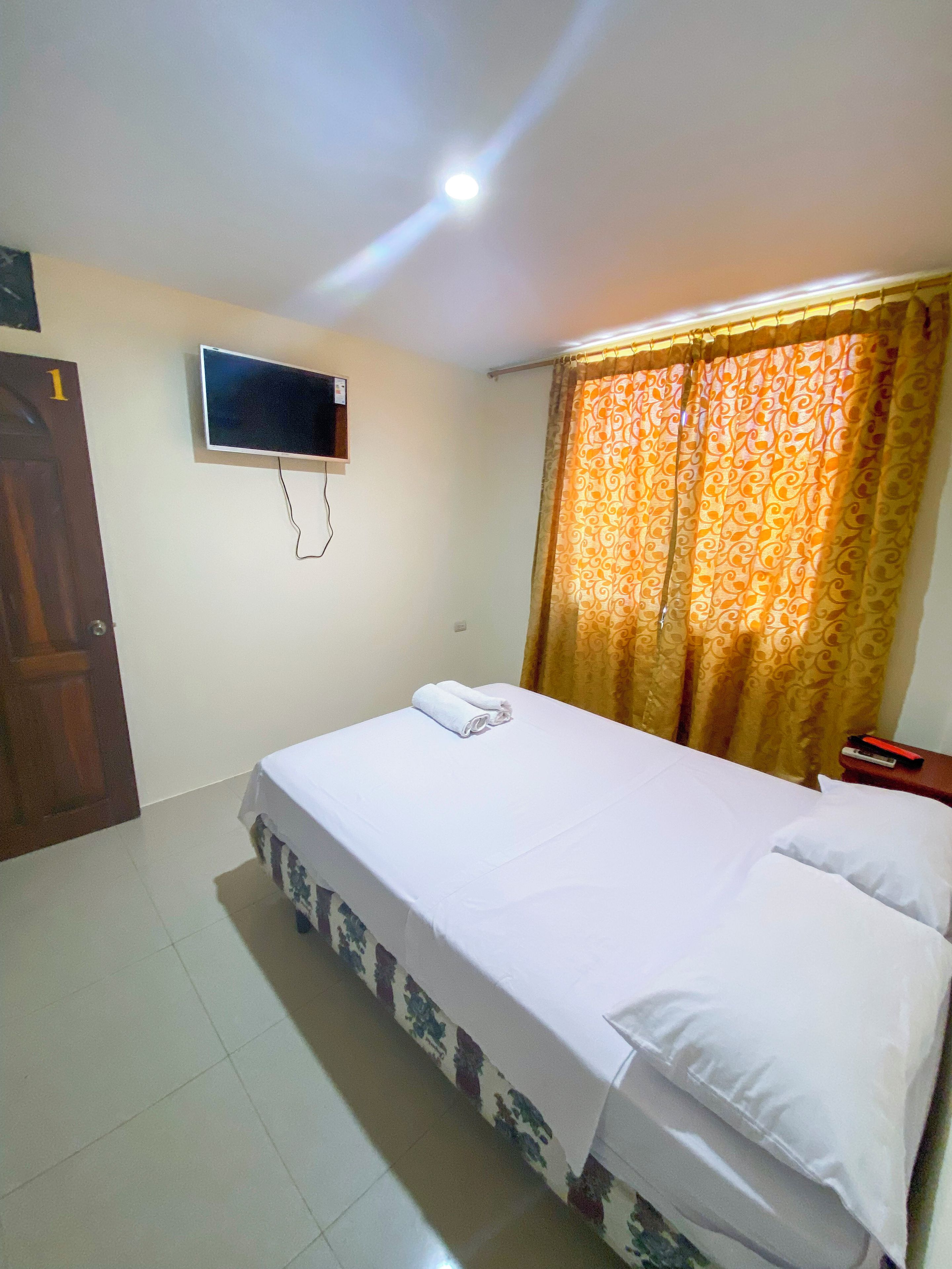 A hotel room with a bed, a TV mounted on the wall, a curtain, and a door.
