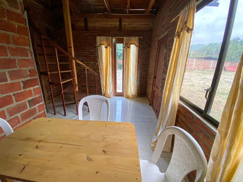 A room with a wooden table and chairs, a brick wall, a window with curtains, and a view outside.