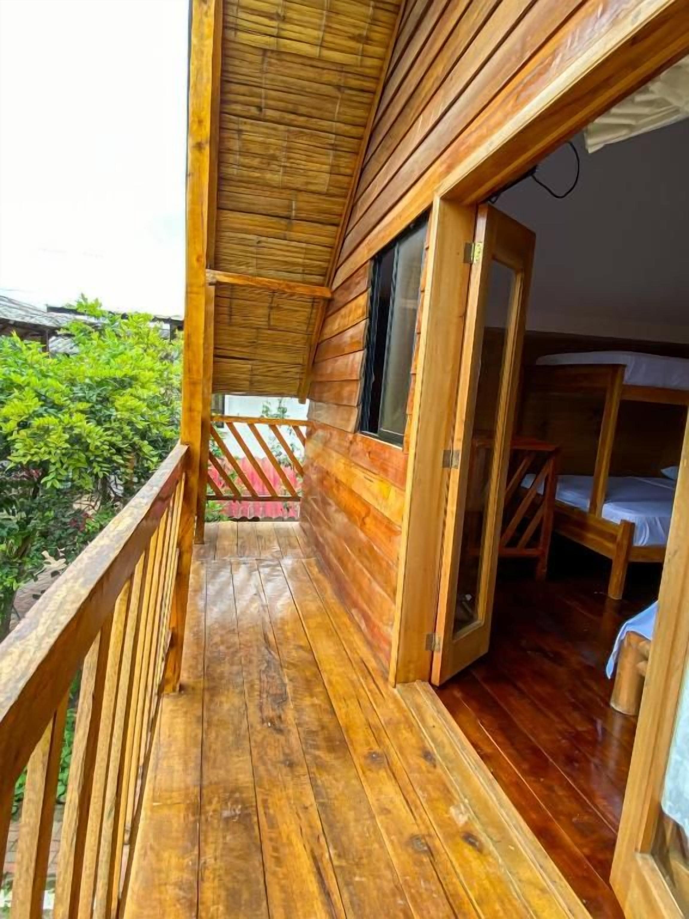 A wooden cabin with a balcony, a wooden door, and a bed.