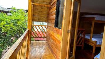 A wooden cabin with a balcony, a wooden door, and a bed.