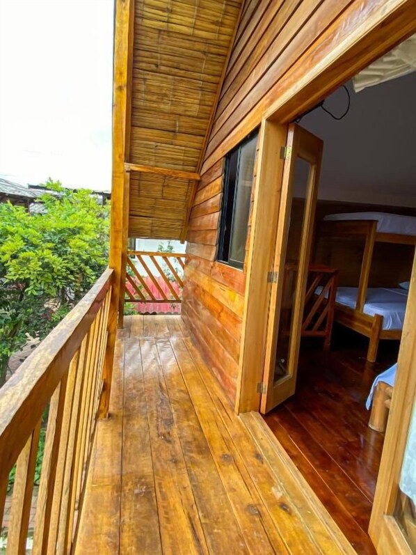 A wooden cabin with a balcony, a wooden door, and a bed.