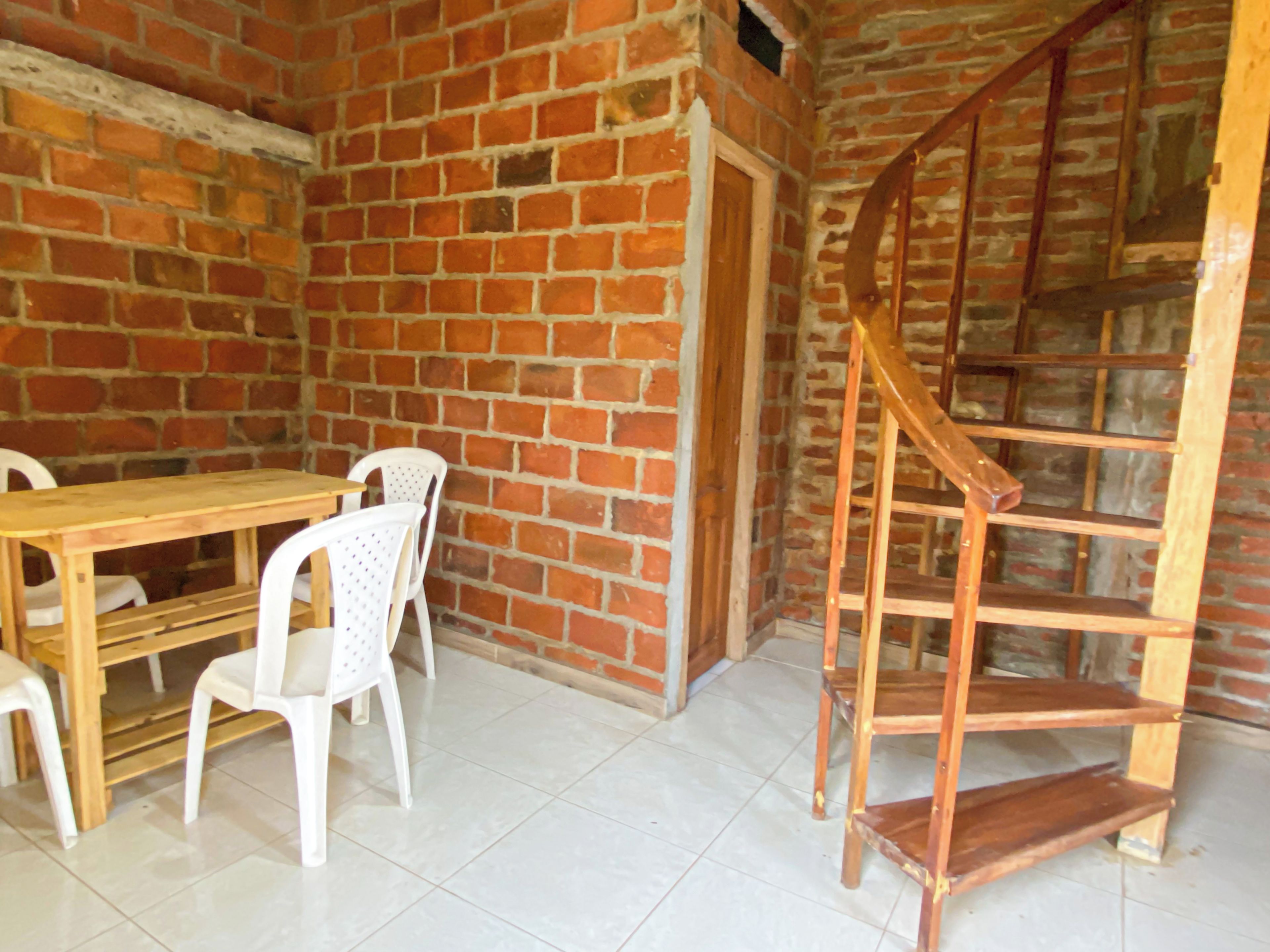 A room with a brick wall, a wooden table with chairs, and a wooden spiral staircase.