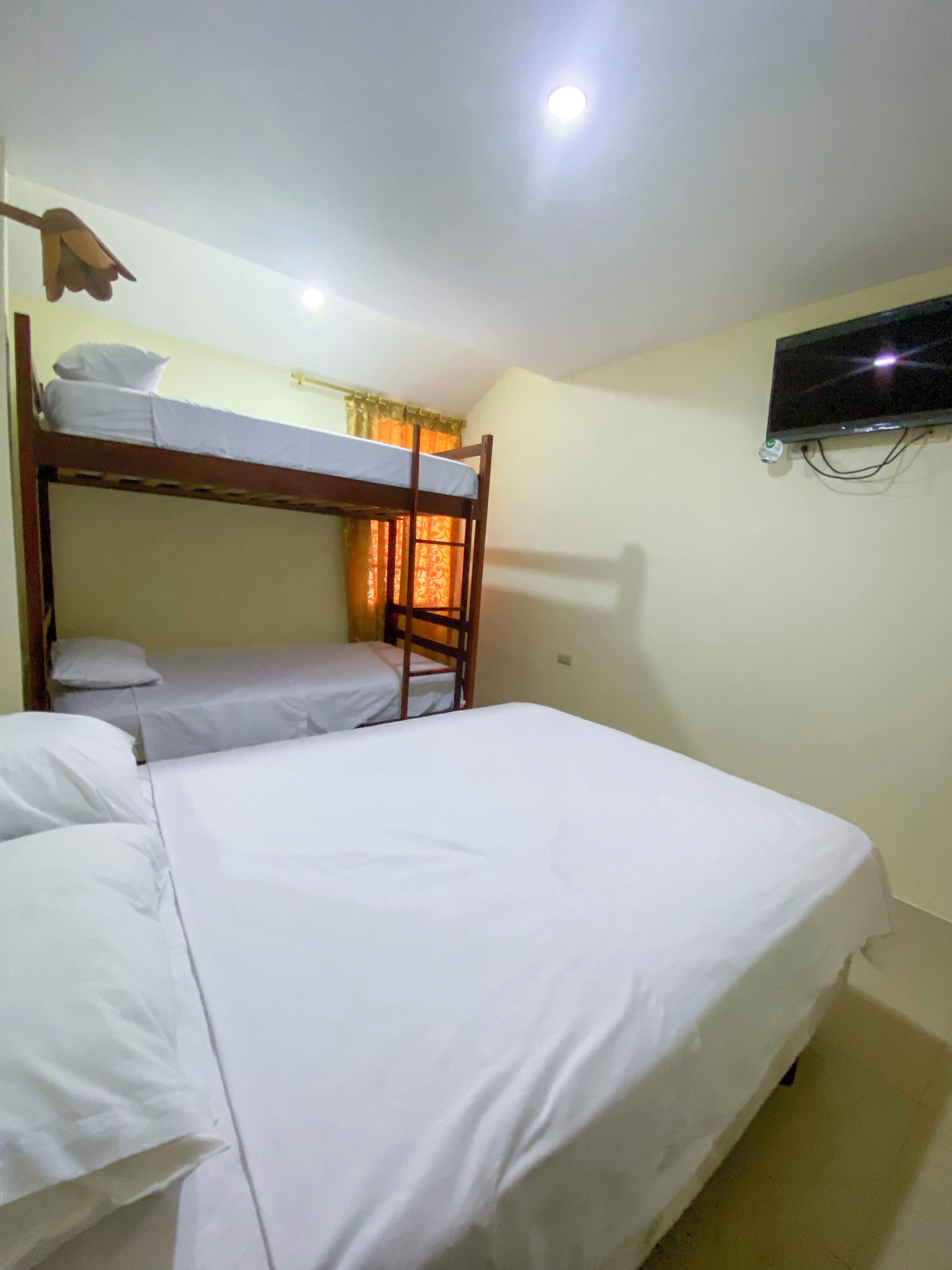 Quarto com beliche, cama de casal, televisão na parede e luminária de teto.