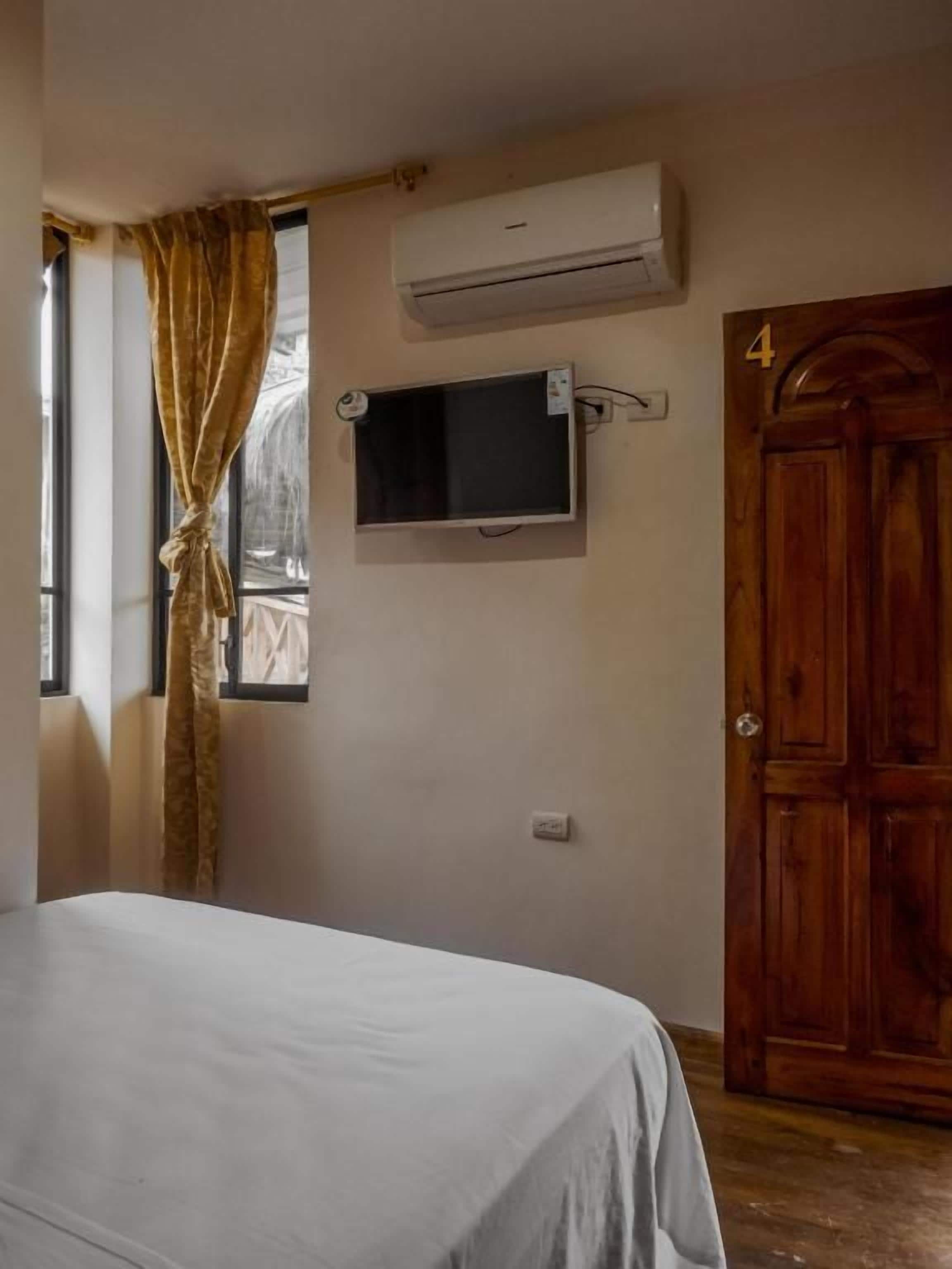 A room with a bed, an air conditioning unit, a television mounted on the wall, and a wooden door with a number.