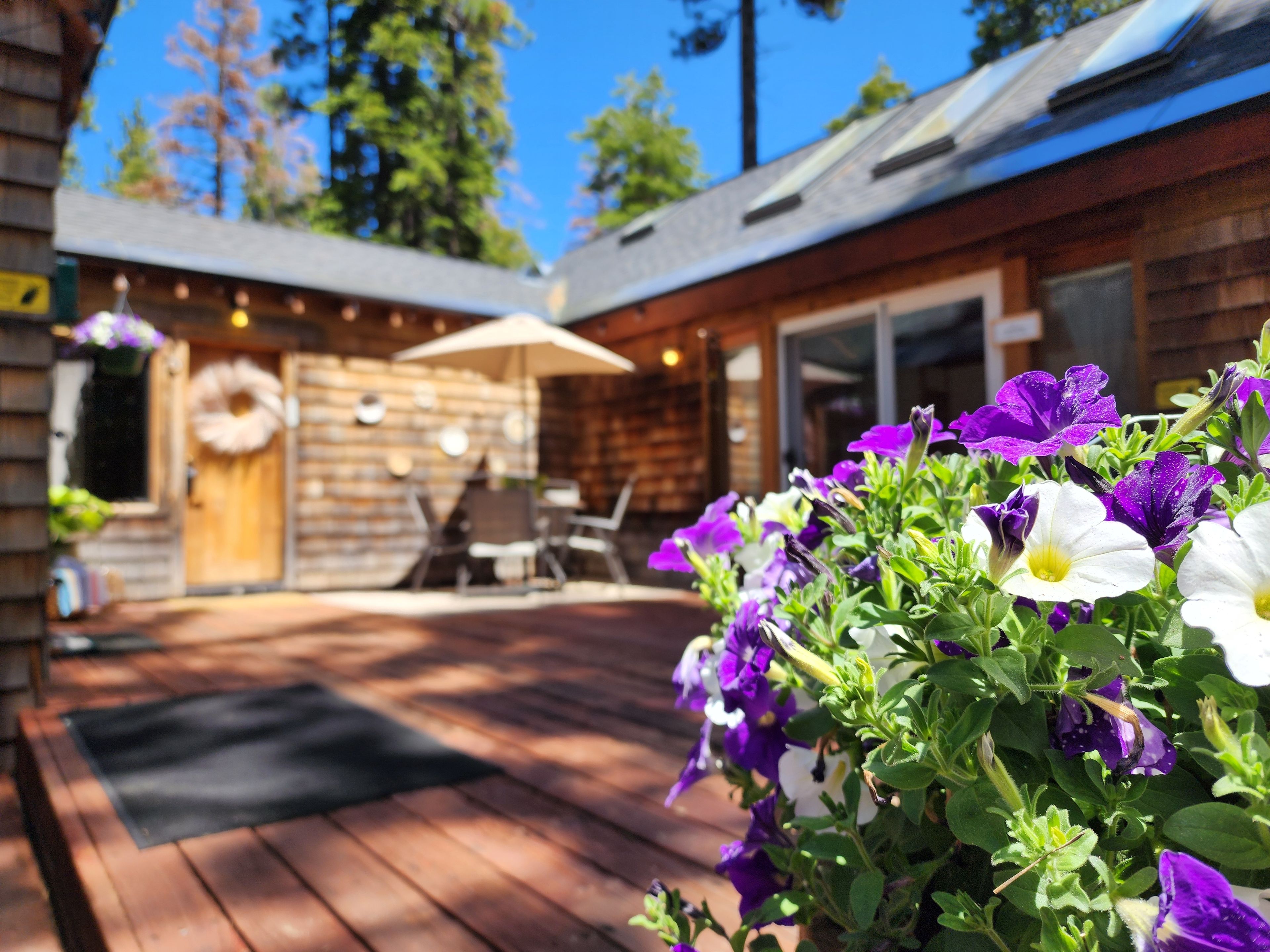 A wooden deck with outdoor furniture, a door with a wreath, and a flower bed with purple and white flowers.
