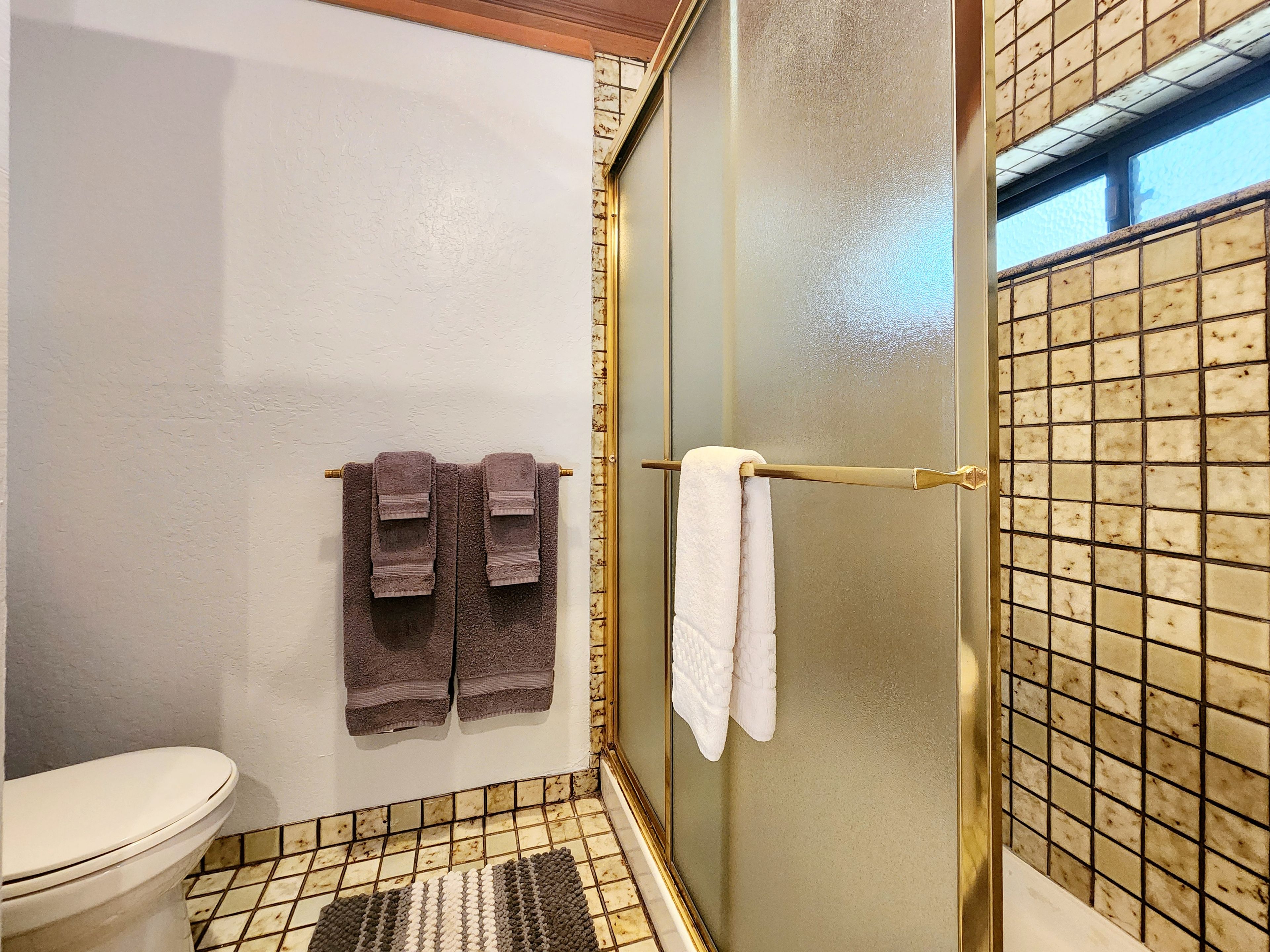 A bathroom with a toilet, a shower with a glass door, and two towels hanging on a towel rack.