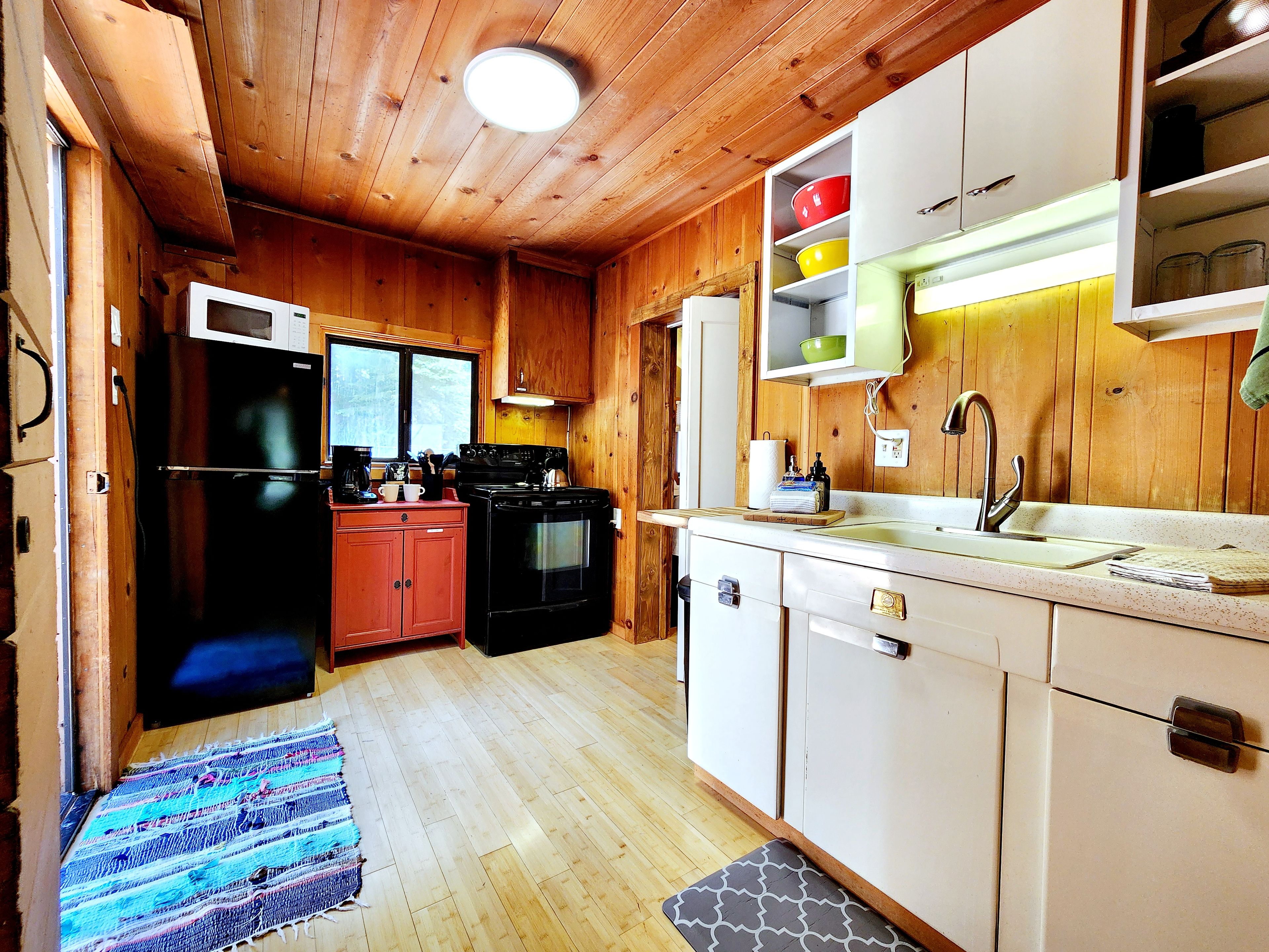 A compact kitchen with wooden walls, a black refrigerator, a stove, and a sink.