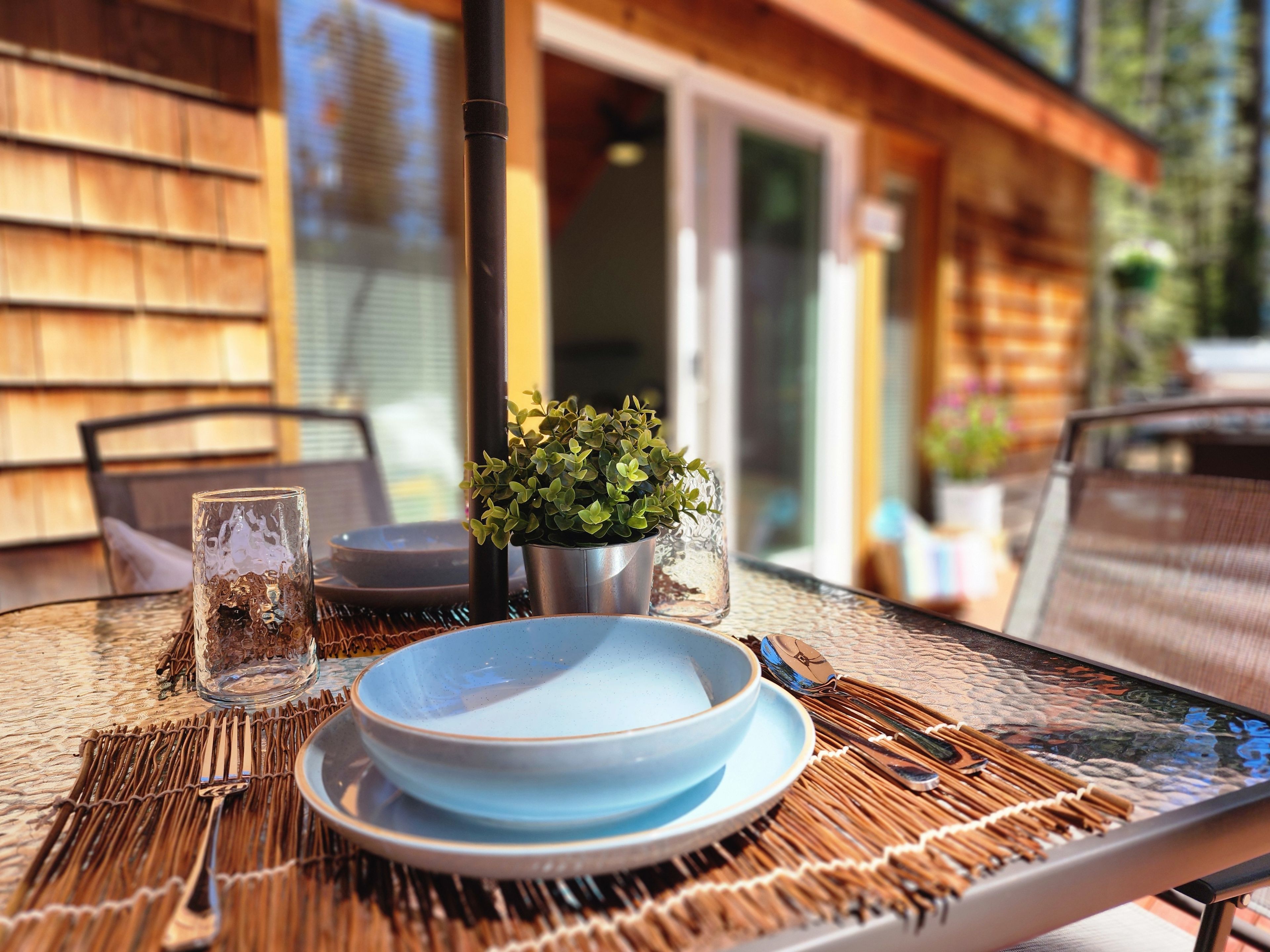 Een terras met een eettafel gedekt voor twee personen, inclusief borden, bestek en glazen.