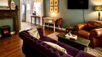 Ein Wohnzimmer mit violettem Sofa, Kamin, Essbereich mit Tisch und Stühlen sowie einem an der Wand befestigten Fernseher.