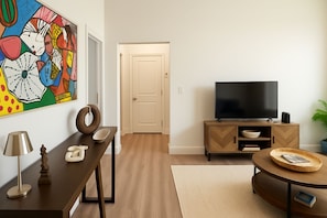 Un salon moderne avec un téléviseur à écran plat, une table basse en bois, une table à manger avec des chaises et un tableau abstrait aux couleurs vives accroché au mur.