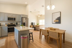 A modern kitchen with stainless steel appliances, a dining area with a wooden table and wicker chairs, and a ceiling fan.