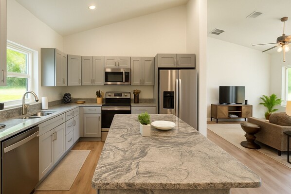 A modern kitchen with stainless steel appliances, a marble island, and a dining area with a sofa.