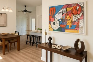 A modern kitchen with a dining area, featuring a wooden table, bar stools, and a decorative wall piece.