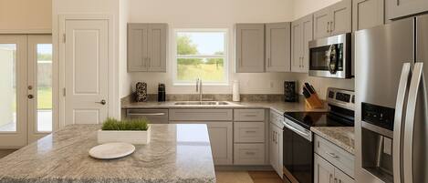 A modern kitchen with a granite countertop, stainless steel appliances, and a view of the outdoors.