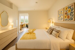 A hotel room with a bed, bedside tables, a dresser, a desk with chairs, and a view of the outdoors.