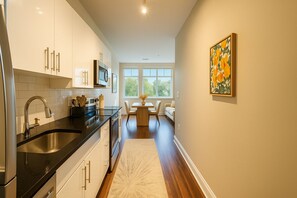 A modern kitchen with a black countertop, stainless steel sink, and white cabinets. There is a dining area with a table and chairs, and a window providing natural light. - Modern Alexandria 1BR | Pool, Gym & Shops (Alexandria)