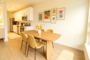 A modern kitchen with white cabinets, a dining table with chairs, and artwork on the wall.