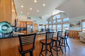 A spacious kitchen with wooden cabinets, a large island with bar stools, and a view through the windows. - Resting Hearts - 4x4 Carova Beach, Ocean Views, Pool, Cargo Lift, Up to 4 Dogs OK, Flex Stays (Carova Beach)