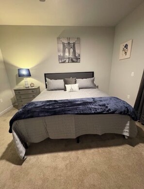 A bedroom with a bed, a nightstand, a lamp, and a wall-mounted picture. - Luxury 1 Bed + Den • Near IMG Academy • Heart of Bradenton (Bradenton)