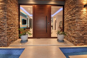 Una entrada moderna con puerta de madera, plantas en macetas y zona de piscina.