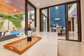 Un interior moderno con comedor, vista a la piscina y una botella de vino sobre una bandeja.