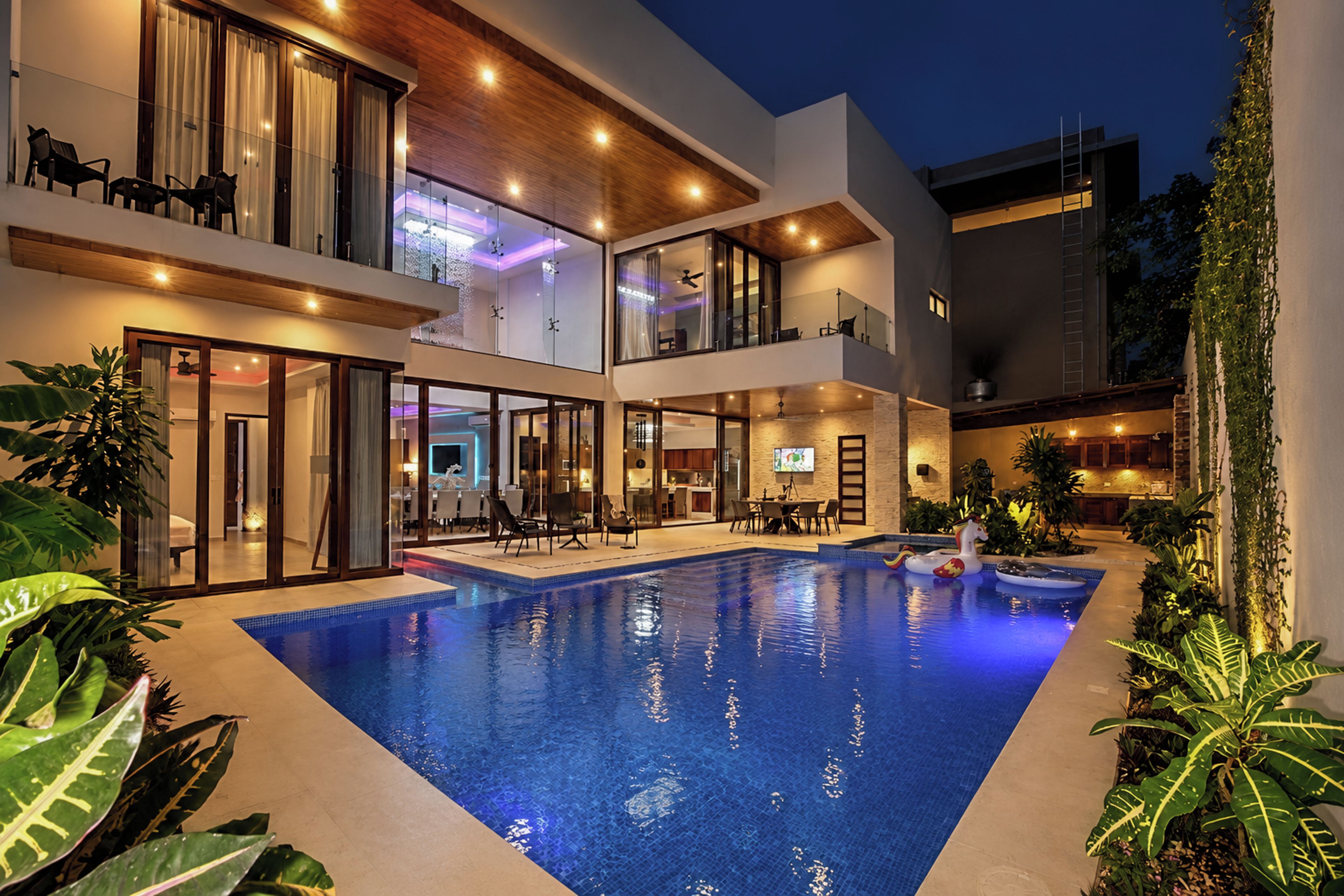 Un edificio moderno de varios pisos con piscina, puertas de vidrio y mobiliario exterior.