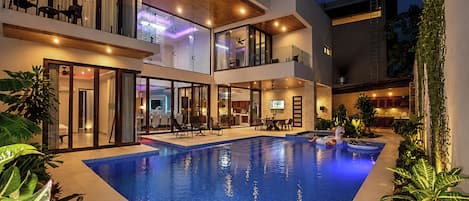Un immeuble moderne à plusieurs étages, doté d’une piscine, de portes vitrées et d’un espace extérieur aménagé pour s’asseoir.