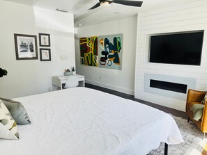 A bedroom with a large bed, a TV, artwork on the wall, and a fireplace. - Furnished 5BR/3BA Home in Bayshore Beautiful — 30-Day Minimum (Tampa)