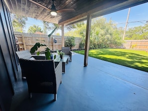 An outdoor patio with wicker furniture and potted plants, a covered area with a ceiling fan, and a view of a well-maintained lawn and trees. - Furnished 5BR/3BA Home in Bayshore Beautiful — 30-Day Minimum (Tampa)