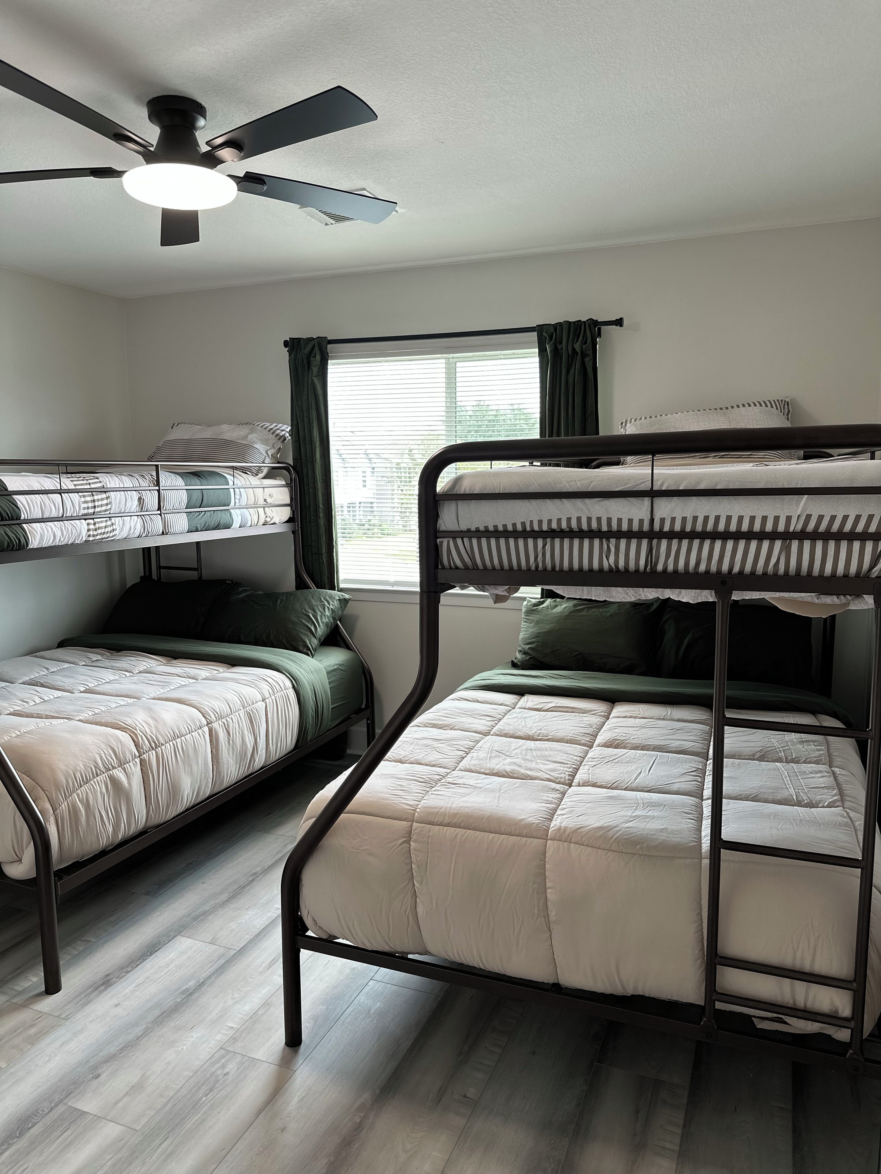 A room with bunk beds, a ceiling fan, and a window with curtains.