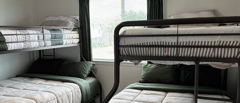 A room with bunk beds, a ceiling fan, and a window with curtains.