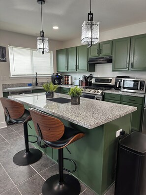 A kitchen with green cabinets, granite countertops, a central island with bar stools, and modern appliances. - Huge Modern 4Bdr home-The Xperience #2 (Houston)