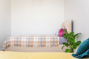 A bed with a plaid bedspread, a yellow throw blanket, and a potted plant beside it. - Apartments Nukus avenue Tashkent (Tashkent)