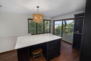 A modern kitchen with a large island, dark cabinetry, a hanging light fixture, and a view of a balcony with a railing. - Spacious and luxurious home on Table Rock Lake (Shell Knob)