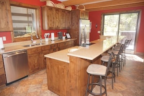 Cozinha com armários de madeira, geladeira de aço inoxidável, uma ilha grande com banquetas e uma lava-louças.