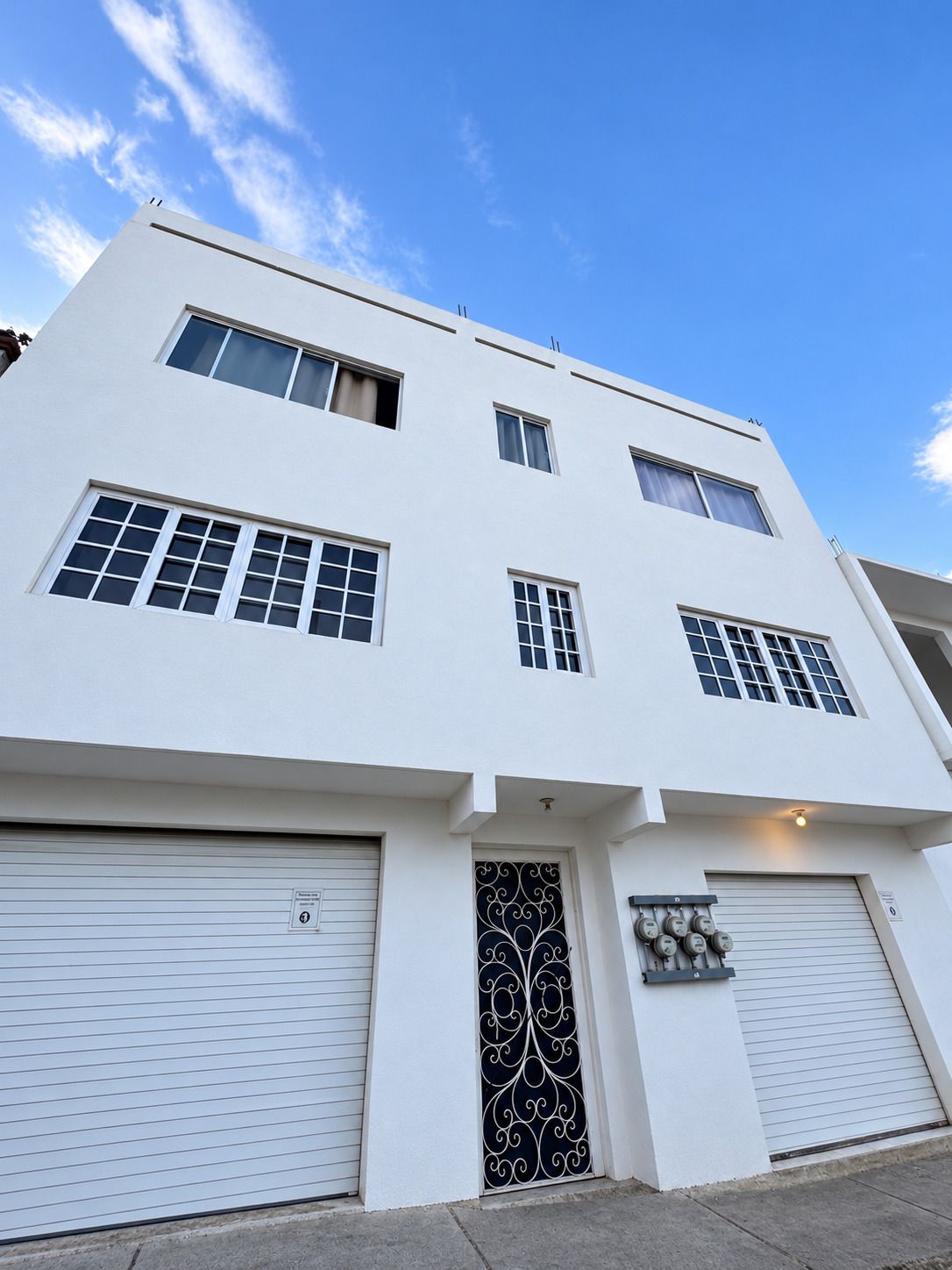 A modern two-story building with a flat roof, large windows, and garage doors.