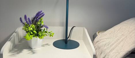 A bedside table with a lamp, a potted plant, and a drawer.