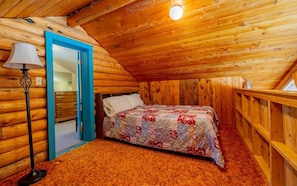 A cozy log cabin bedroom with a bed, a dresser, and a lamp. - The Lodge at Wapiti Valley Ranch- ideally located between Cody and Yellowstone (Cody)