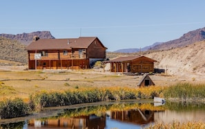 A wooden cabin with a porch, a smaller attached structure, and a pond in front. - The Lodge at Wapiti Valley Ranch- ideally located between Cody and Yellowstone (Cody)