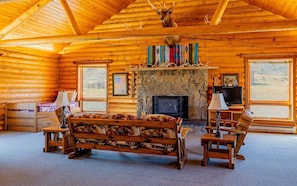 A log cabin interior with a fireplace, a bed, a television, and a deer head mounted on the ceiling. - The Lodge at Wapiti Valley Ranch- ideally located between Cody and Yellowstone (Cody)