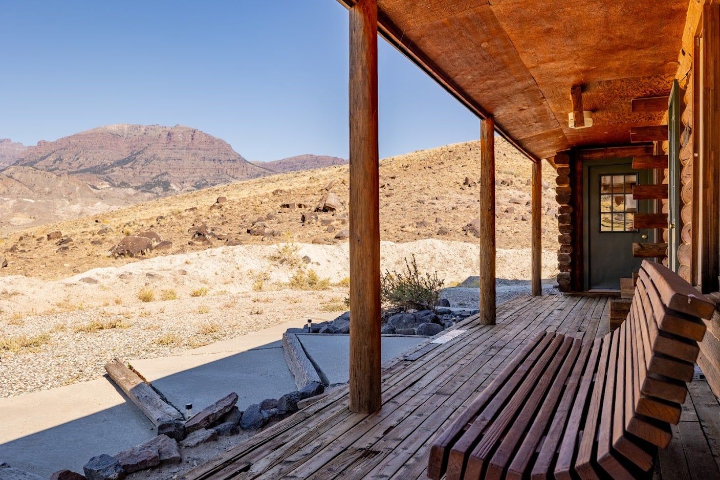 Un porche de madera con un banco, una chimenea y vistas a un paisaje desértico con montañas al fondo.