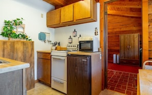 A compact kitchen with wooden cabinets, a stove, a microwave, and a refrigerator. - The Cabin at Wapiti Valley Ranch- ideally located between Cody and Yellowstone (Cody)