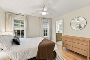 Quarto com cama, cómoda de madeira, ventoinha no teto e janela com persianas.