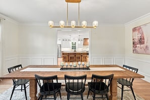 Uma sala de jantar com uma grande mesa de madeira, cadeiras pretas e um candelabro.