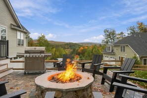 A patio with a stone fire pit, outdoor grill, and seating area with chairs and tables. - Luxury Owl’s Nest Retreat Golf & Resort (Campton)