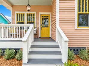 Une maison avec une porte jaune, des balustrades blanches et une véranda avec des chaises.