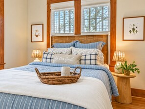 A bedroom with a bed, two bedside lamps, a bedside table with a plant, and a framed botanical illustration on the wall. - The Mustard House - Featured on Restoring Galveston (Galveston)
