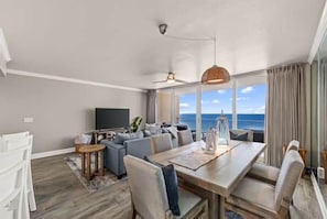 A modern living room with a dining area, a flat-screen TV, and a view of the ocean. - New Listing! Newly Renovated With ALL Brand New Furnishings! (Panama City Beach)