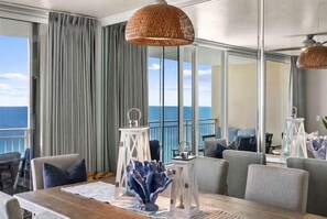 Uma sala de jantar com mesa, cadeiras e vista para o mar.