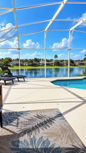 Un espacio al aire libre cubierto con piscina, sillas de descanso y vistas a un lago y casas al fondo.